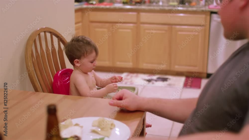 An adorable little boy in a high chair booster seat eating messy food, dinner time with family An adorable little boy in a high chair booster seat eating messy food, dinner time with family