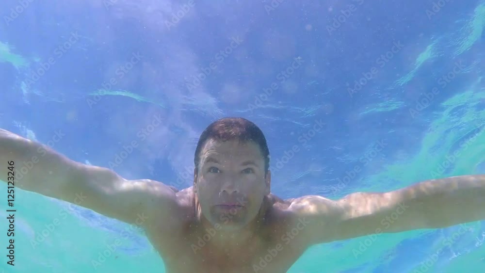 Slow motion 60 fps underwater low angle shot of muscular Caucasian man swimming breast stroke with eyes open under surface of sea Slow motion 60 fps underwater low angle shot of muscular Caucasian man swimming breast stroke with eyes open under surface of sea
