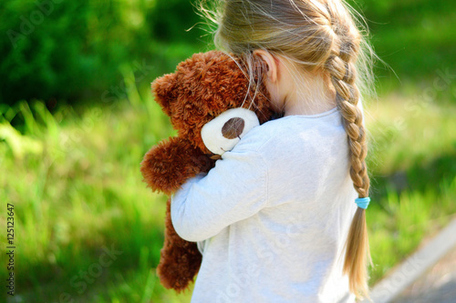 Adorable sad girl with teddy bear in park.