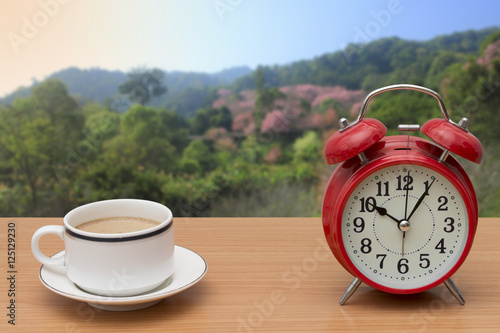 coffee and alarm clock on wooden table with nature background