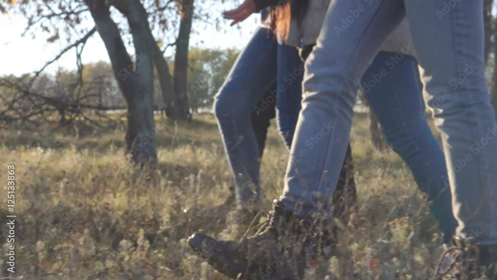 Close up on feet of unidentifiable people in rugged pants walking through wild grass opposite the sun at sunset side view Close up on feet of unidentifiable people in rugged pants walking through wild grass opposite the sun at sunset side view
