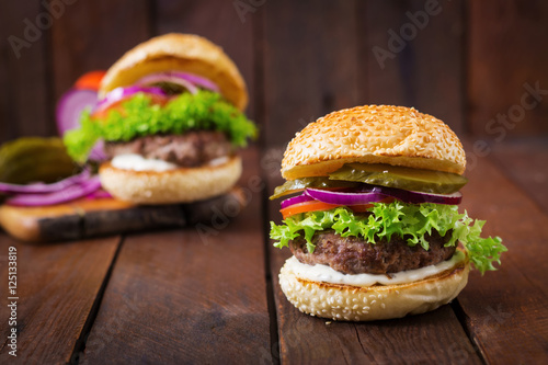 Big sandwich - hamburger burger with beef, pickles, tomato and tartar sauce on wooden background.