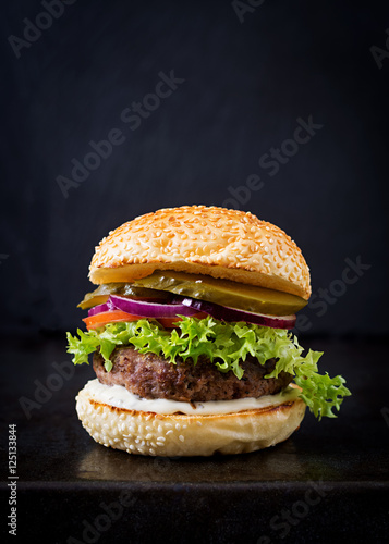Big sandwich - hamburger burger with beef, pickles, tomato and tartar sauce on black background.