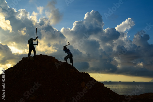 Workers using hoe to dig heap of soil