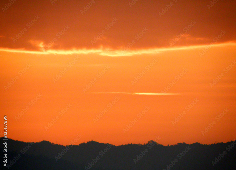 Orange gradation of sunset cloudy sky over the silhouette of mountain range, Thailand