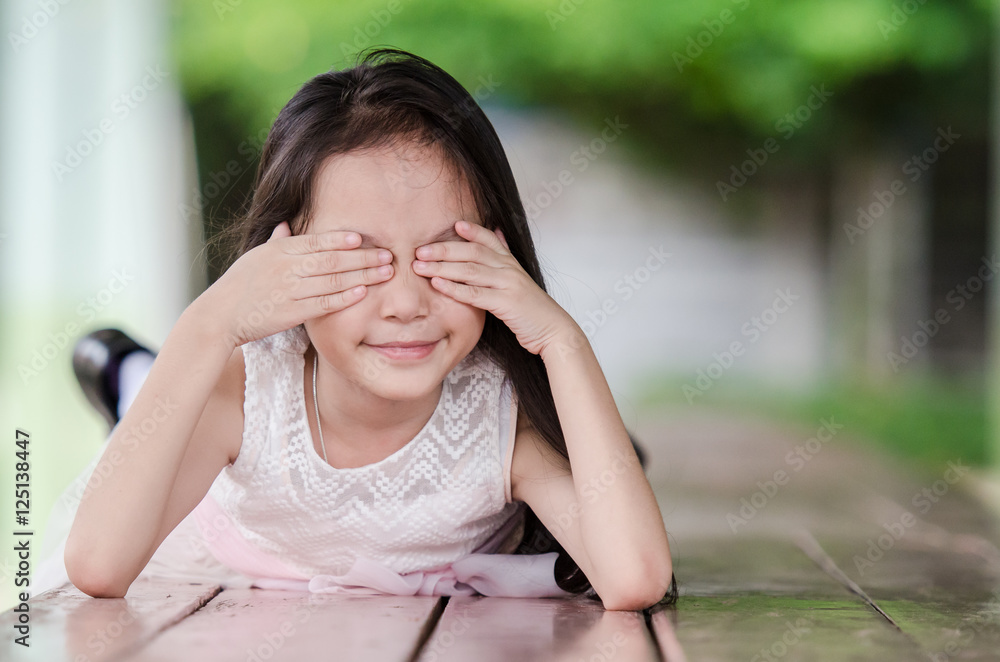 Portrait of a little girl in pink dress closing her eyes and lyi