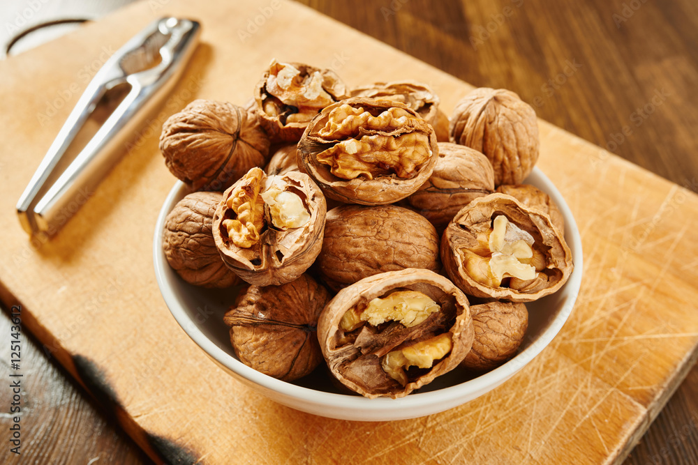 Walnuts in bowl and nutcracker on a cutting board and wooden table Walnuts in bowl and nutcracker on a cutting board and wooden table