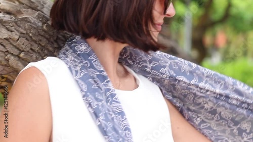 Happy young woman in white dress with sunglasses and balinese silk scarf whirling at the beach. Slow motion. Bali, Indonesia.