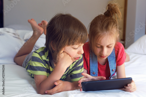 Cute little boy and girl playing with tablet on bed