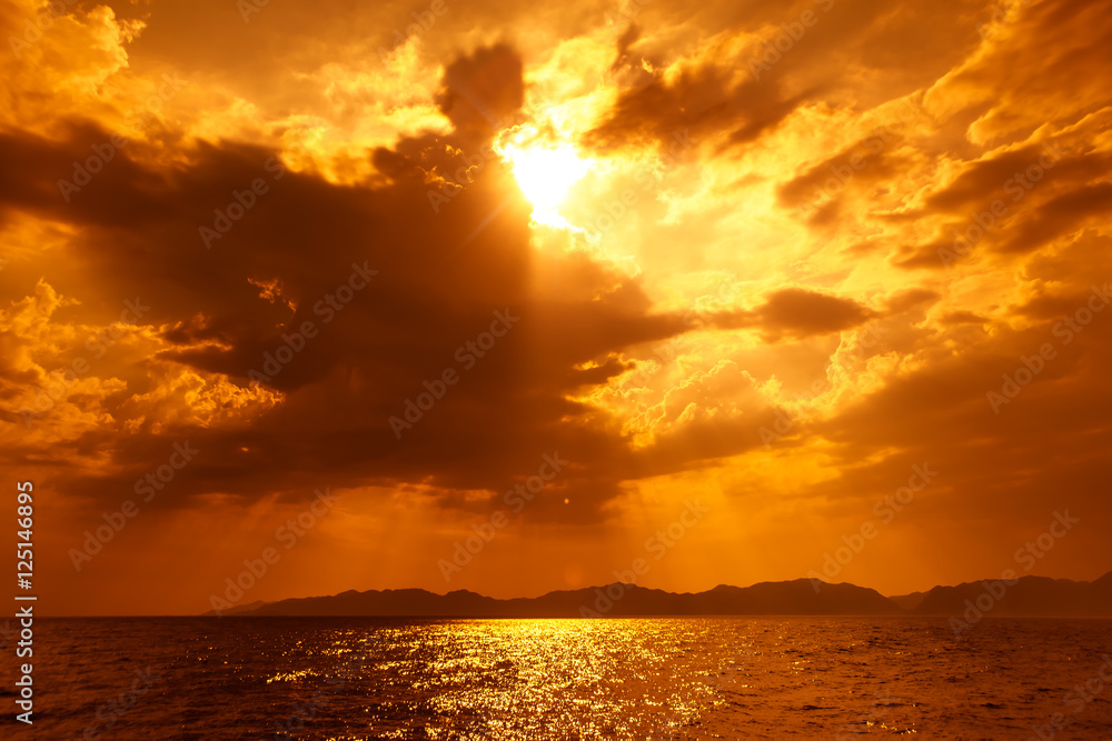 Naklejka premium Złocisty rozbłysk słońca między chmurami na morskim horyzocie