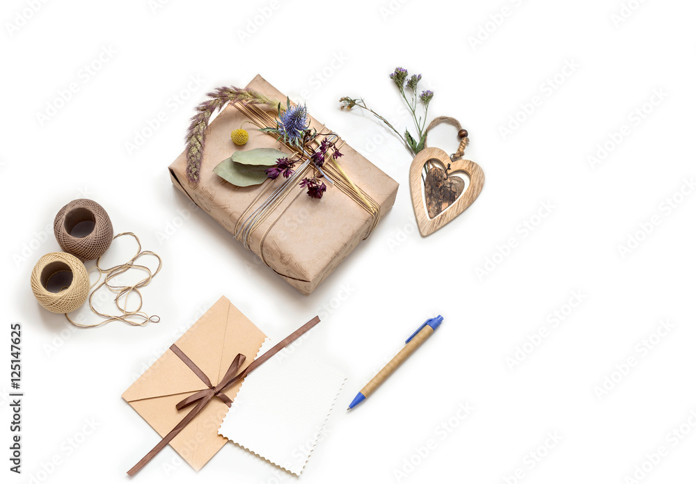 Beautiful handmade gift box (package) with flowers, envelope with blank gift tag and decorative rope on white background. Wooden hart. Vintage Style. BOHO Beautiful handmade gift box (package) with flowers, envelope with blank gift tag and decorative rope on white background. Wooden hart. Vintage Style. BOHO