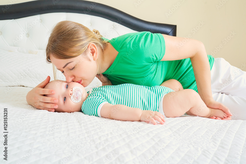 Mom with baby on white bed. Mother kissing her child. Family con Mom with baby on white bed. Mother kissing her child. Family con