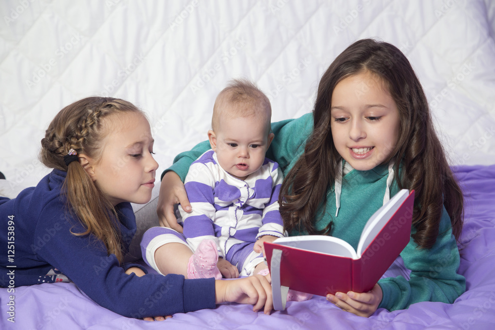 Three sisters, baby and two older sisters reading book in the bed. Bedtime story.. Three sisters, baby and two older sisters reading book in the bed. Bedtime story..