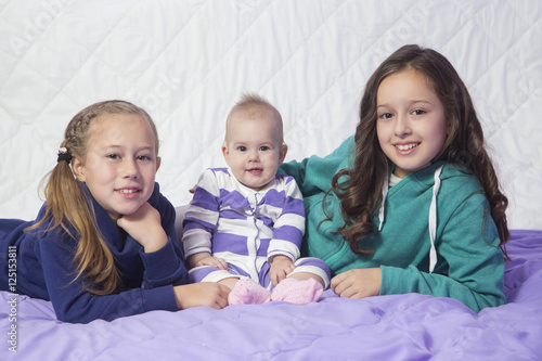  Three sisters, baby and two older sisters playing in the bed. .