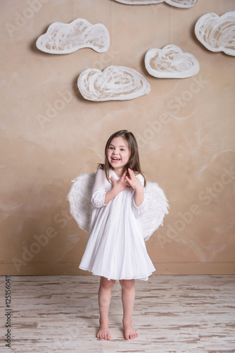 little angel girl in white dress with white wings under the clouds