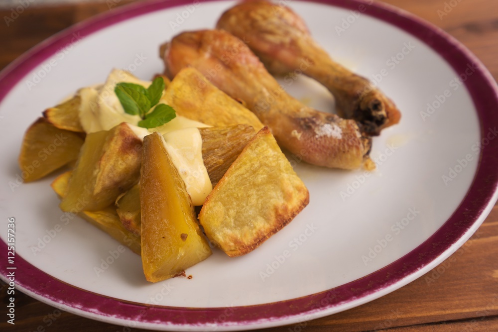Roasted chicken drumsticks served on the old vintage porcelain plate with baked sweet potatoes and french mustard sauce. Picture isolated on the wooden table closeup. Fresh and healt family lunch.