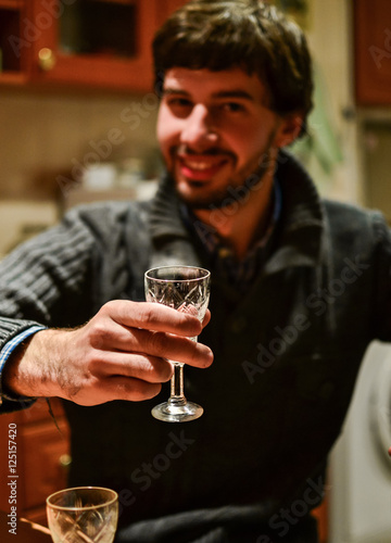 Young unshaven man holding glass of strong alcoholic drink vodka