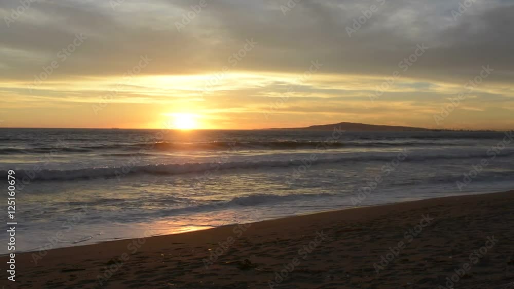 A sunset in Huntington Beach, California shows the ocean waves and orange glow of the sun. A sunset in Huntington Beach, California shows the ocean waves and orange glow of the sun.