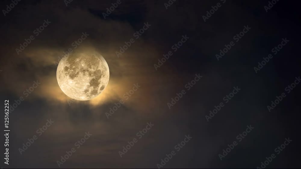 Fog moves across a full moon framed against a dark moody, amber sky with cloud cover.. Fog moves across a full moon framed against a dark moody, amber sky with cloud cover..