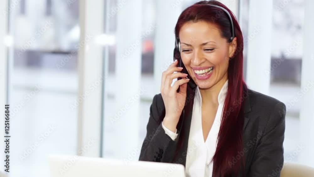 Woman with headphone talking,using a laptop computer and holding a cup of hot drink Woman with headphone talking,using a laptop computer and holding a cup of hot drink