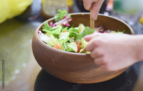 Fotografiet Healthy green salad being tossed in wooden bowl on counter