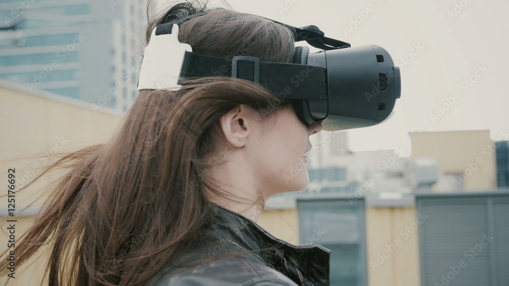 Brunette woman girl with waving hair uses a virtual reality glasses on the roof. 4k