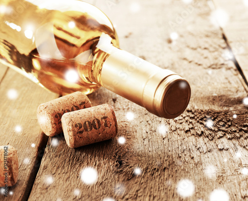 Bottle of white wine with corks on wooden background, closeup. Snowy effect, Christmas celebration concept.