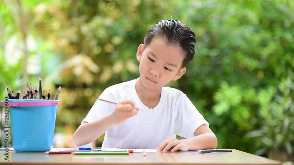 Young Asian boy write on the note book by color pencil in the garden Young Asian boy write on the note book by color pencil in the garden