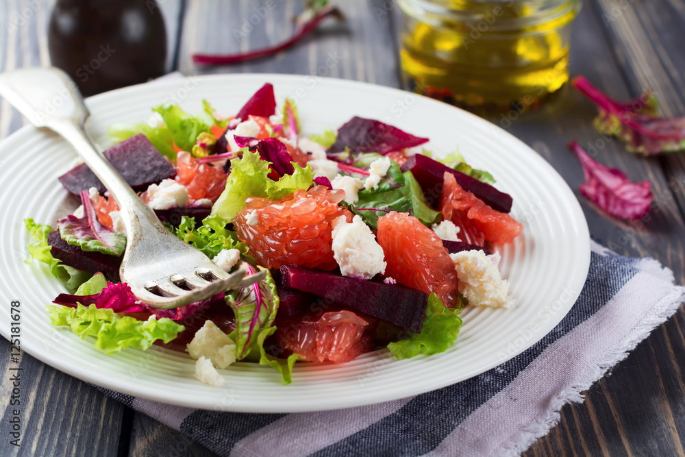 Salad of beets, lettuce, beetroot leaves, grapefruit and feta cheese on the old wooden background. Selective focus.