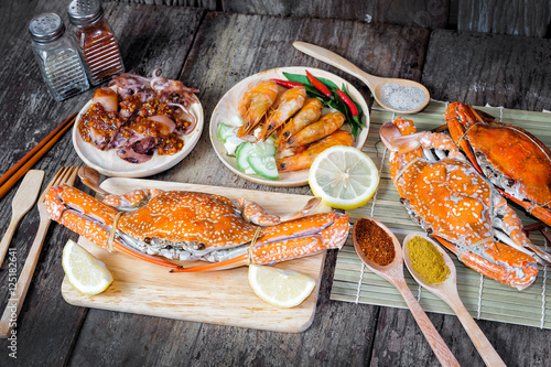 Delicious grilled seafood (jumbo crabs, prawns, squids) with spices on wood table