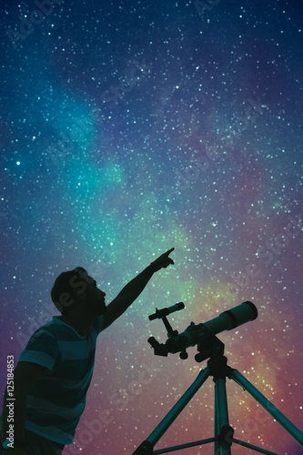 Man looking at the stars with telescope beside him and countryside silhouettes.