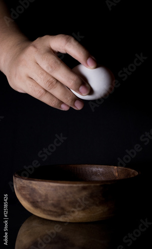Close-up of hands cracking egg and wood bowl on Black