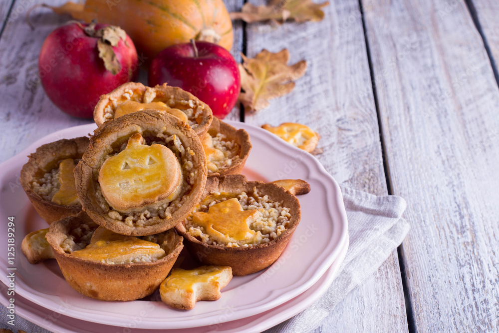 Delicious Tartlets mini tarts pie with pumpkin and apple for Halloween in a pink plate on wooden background Delicious Tartlets mini tarts pie with pumpkin and apple for Halloween in a pink plate on wooden background