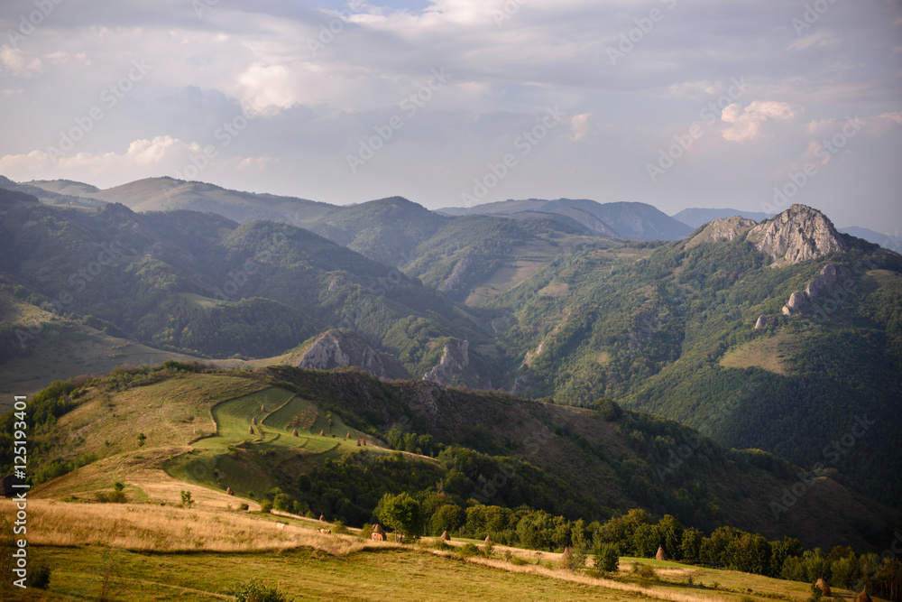 Amazing Romanian countryside in mountains with haystacks on pasture in the summer afternoon light
