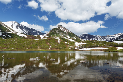 Summer landscape of Kamchatka: view of Mountain Range Vachkazhets and clouds in blue sky, reflection in mountain lake on sunny day. Eurasia, Russian Far East, Kamchatka Peninsula.