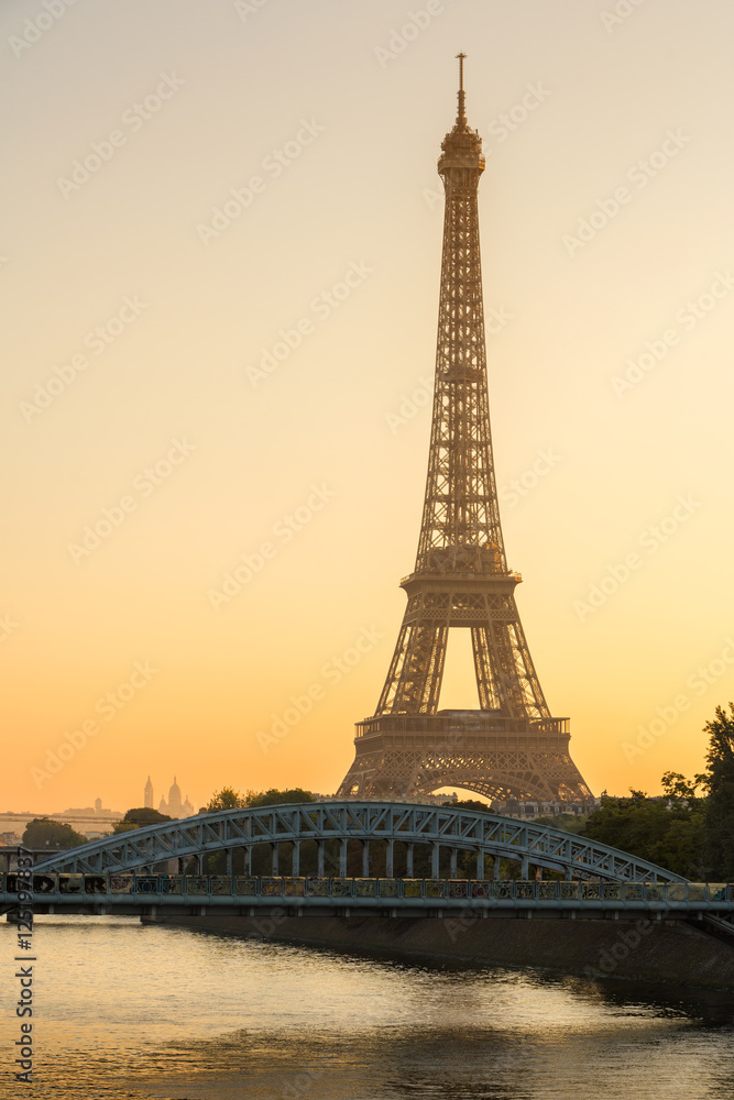 Warm sunrise light on the Eiffel Tower and the Seine River in Paris, France. The view includes the Pont Rouelle bridge and in the distance, the Basilica of the Sacred Heart (Sacre Coeur).