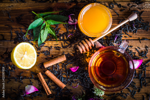 A cup of black tea. Honey, cinnamon, lemon, tea leaves, mint. On a wooden background.