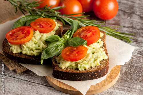 Avocado toast, cherry tomato on wooden background. Breakfast with toast avocado, vegetarian food, healthy diet concept.