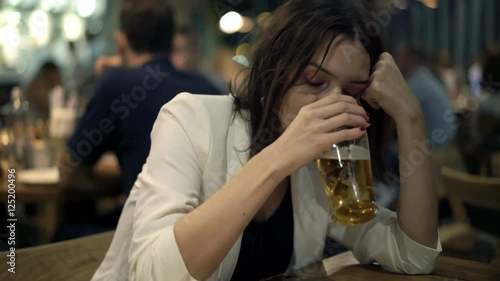 Drunk, sad woman drinking beer while sitting in the bar, 4K 

