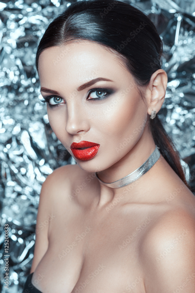 Portrait of beautiful young lady with luxury makeup and stylish accessory on her neck. Holiday makeup on silver bright shiny background.