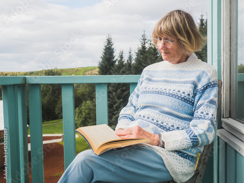 Vászonkép Senior woman is reading at a balcony
