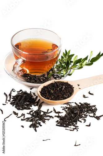 Black tea in a glass cup. Tea leaves in wooden spoon. On white, isolated background.