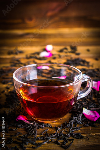 A cup of black tea. Tea leaves with rose petals. On a wooden background.