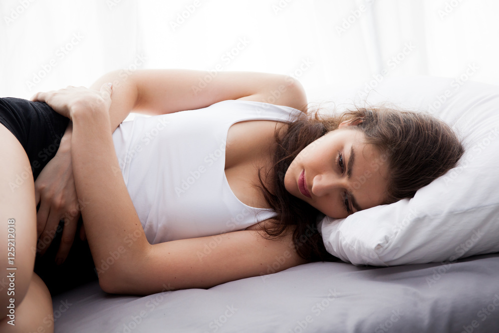 Young beautiful Caucasian woman on bed being sad, depressed, having stomach pain, having food poisoning, cramps sickness Young beautiful Caucasian woman on bed being sad, depressed, having stomach pain, having food poisoning, cramps sickness