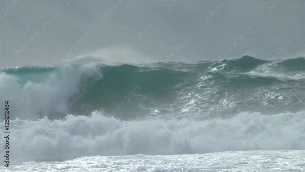 Massive waves rolling in at a surf break at the Atlantic ocean at ongoing thunderstorm. Light beams of sun on some parts of the sea.