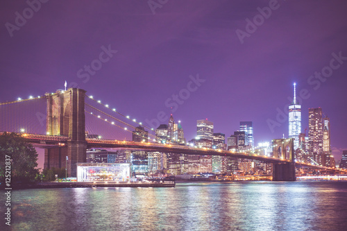 New York City skyline and Brooklyn Bridge at night with light and vintage toned filter effect