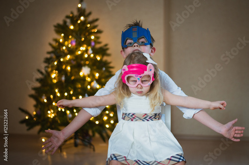 брат и сестра в смешных масках у новогодней елки