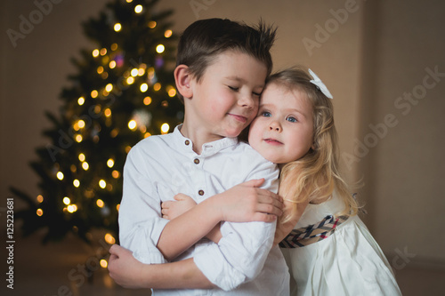 брат и сестра обнимаются у новогодней елки