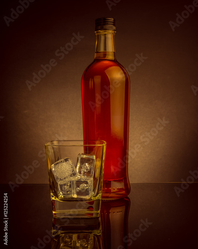 whiskey with ice cubes in glass near bottle on black background, warm atmosphere, time of relax with whisky