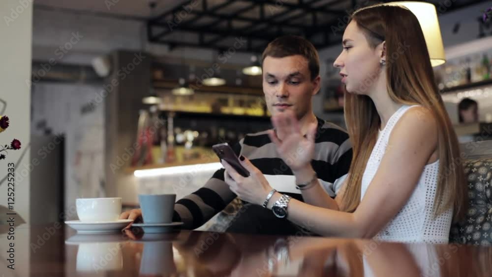 Attractive young couple talking and using smartphone at cafe Attractive young couple talking and using smartphone at cafe